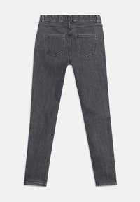 Στενά τζιν σκούρου γκρι χρώματος με ελαστική μέση και δύο πίσω τσέπες, απλωμένα επίπεδα σε λευκό φόντο.