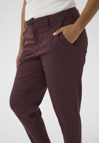 Burgundy trousers with a smooth texture, featuring a button closure, side pockets, and a tailored fit.