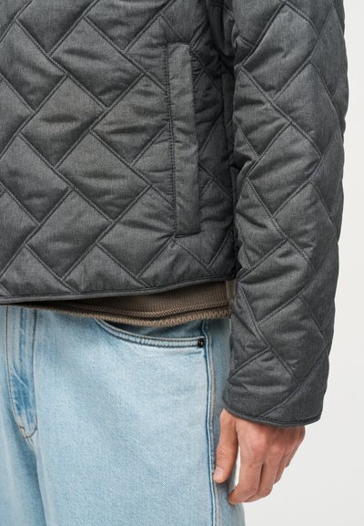 Άτομο που φοράει σκούρο γκρι μπουφάν με επένδυση και πλαϊνή τσέπη, ανοιχτό μπλε τζιν και ορατό καφέ πλεκτό τελείωμα πουλόβερ.