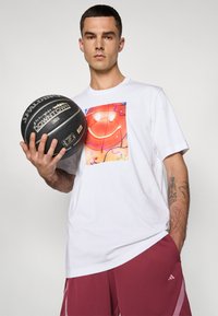Witte katoenen T-shirt met een kleurrijke gedrukt afbeelding aan de voorkant, gecombineerd met bordeauxrode shorts met zijstrepen en een Adidas-logo.