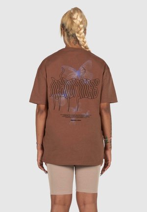 Hnedé oversized tričko s motýľom v modrej a čiernej farbe na chrbte, s krátkymi rukávmi a voľným strihom.