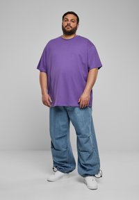 Tricou oversized violet, din material bumbac, cu mâneci scurte. Purtați cu blugi largi de un albastru deschis, cu manșete elastice. Tenisi albi.