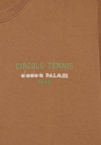 T-shirt in cotone marrone con testo verde e bianco: "CIRCOLO TENNIS diadora PALMES 1948." Texture liscia con scollatura rotonda.