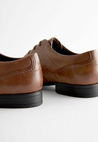 Chaussures en cuir marron avec une texture lisse, bouts ronds et semelles en caoutchouc noir. Présentent des coutures détaillées et un design classique.