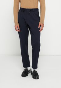 Στρατιωτικό παντελόνι με πιέτες μπροστά, μέση με κορδόνι και ανοιχτόχρωμο υφασμάτινο ύφασμα, σε συνδυασμό με μαύρα μοκασίνια και λευκές κάλτσες.