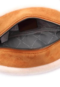 Pochette rotonda con esterno in suede color beige, bordo in peluche beige e rivestimento interno grigio a motivo. La chiusura con zip rivela solo etichette interne minime.