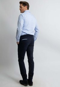 Blauw gestreept shirt met een kraag, donkerblauwe broek en zwarte schoenen. De broek heeft twee achterzakken met blauwe accenten.