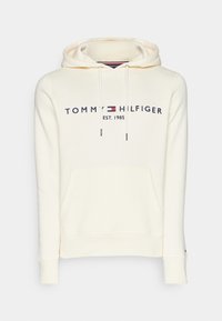 Kremihuppari, jossa on etutasku, nyöritykset ja logo-teksti "TOMMY HILFIGER EST. 1985" tummansinisellä värillä punaisilla ja valkoisilla yksityiskohdilla.