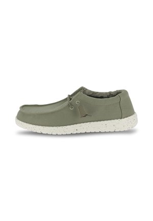 Chaussure en toile verte avec un design à lacets, semelle blanche à pois, et doublure intérieure texturée. Présente un logo discret sur le côté.