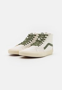 Höga sneakers i krämfärgad canvas med gröna snören och ett grönt sidosträcka. Har en texturerad yta och en gummisula.