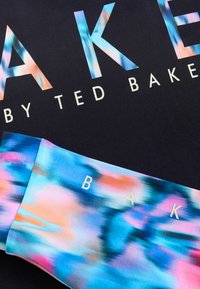 Crni materijal s velikim višebojnim tekstom "BAKE" i "by TED BAKER." Donji dio prikazuje živopisan apstraktni uzorak u plavoj, ružičastoj i breskvastoj boji.