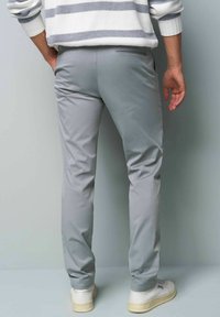 Grijze broek gemaakt van een gladde stof, met een slim fit ontwerp en achterzakken, gecombineerd met witte sneakers.
