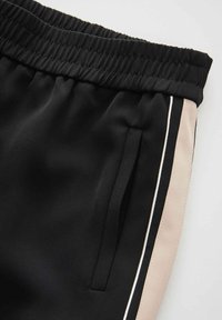 Black athletic pants with a textured waistband, featuring a side beige panel accented by a thin white stripe. Includes side pockets.
