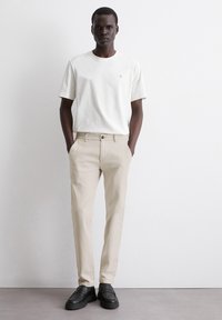 White cotton t-shirt with small logo, paired with beige trousers and black loafers. Simple, streamlined design with a casual fit.