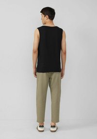 Schwarzes ärmelloses Shirt, lässige Passform, kombiniert mit hellolivgrünen Hosen und weißen Schuhen mit schwarzen Akzenten. Schlichtes, unverziertes Design.