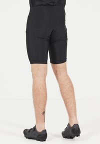 Shorts de cyclisme noirs avec un insert rembourré, texture lisse, coupe ajustée et longueur mi-cuisse, associés à des chaussures de cyclisme noires.