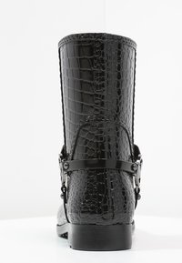 Bottine en cuir noir à texture crocodile, avec une sangle à détail de boucle, un bout arrondi et un talon solide. Fini lisse et brillant.