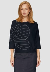 Czarna bluzka z 3/4 rękawami, z białym liniowym wzorem. Wykonana z teksturowanej tkaniny, ma luźny krój i zaokrąglony dół.