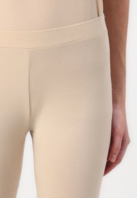 Bežové legíny vyrobené z měkké, elastické látky s hladkým povrchem a elastickým pasem, vykazující přiléhavý siluetu a ploché švy.