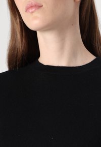Črn pleten pulover z okroglo izrezom. Mehak material, minimalne šive in prilagojena oblika. Poudarek na vratu in ramenskem delu.