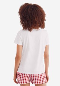 Hvid t-shirt med korte ærmer kombineret med shorts i rød og hvid ternet mønster, set fra ryggen. Glat stof, casual pasform.