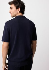 Polo a maniche corte di colore blu navy, in tessuto strutturato, con colletto classico, polsini e orlo a coste, caratterizzato da un motivo sottile sul retro.