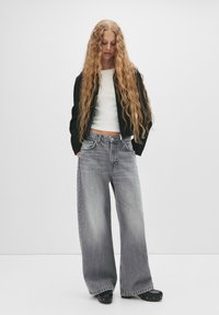Široke sivo denim hlače z zamašenim izgledom, v kombinaciji z oprijeto belo majico in črno bomber jakno, ki ima rebraste manšete in pas.