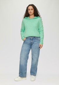 Mintgrüner Kapuzenpullover mit langen Ärmeln, kombiniert mit hellblauen weiten Jeans, abgerundet mit weißen Sneakers.