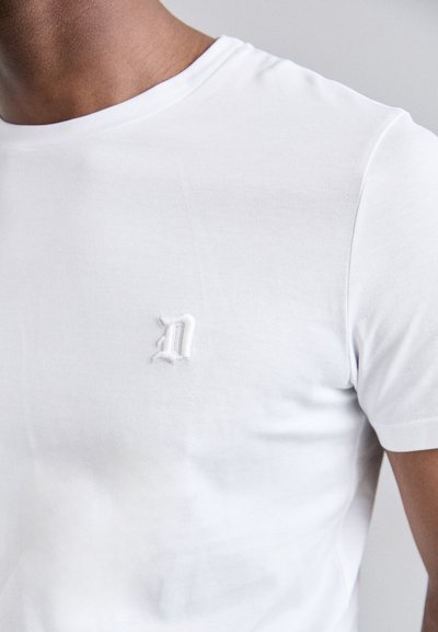 T-shirt en coton blanc avec un col rond et un petit logo brodé sur la poitrine gauche. Texture lisse et design classique.