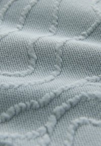 Gros plan sur un tissu tricoté gris clair avec des motifs circulaires en relief et une texture douce tissée.