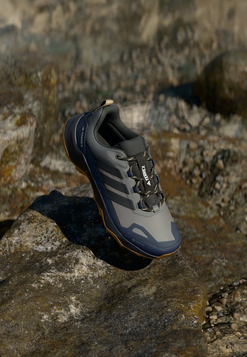 Gray low-top athletic shoe with textured upper, 3 stripes, and contrasting tan sole. Features secure lacing and waterproof design.