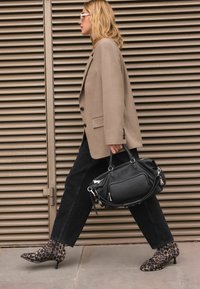 Černá kožená kabelka se stříbrnými prvky, nošená s béžovým oversized blejzrem, tmavými džíny a ankle boots s leopardím potiskem.