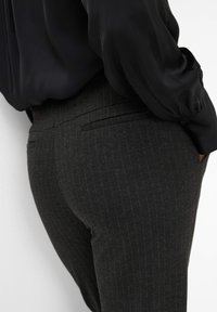 Schwarze gestreifte Hose mit glatter Textur, tailliertem Design und zwei Gesäßtaschen, kombiniert mit einer lockeren schwarzen Bluse.