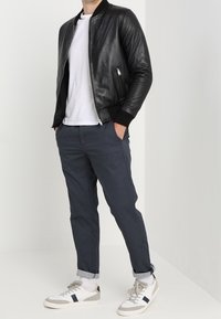 Svart läderbombarjacka med vit t-shirt, marinblå mönstrade byxor och vita sneakers med marinblå detaljer. Har ribbade manschetter och nederkant.