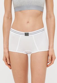 Λευκές boxer κομμένες με φαρδύ ελαστικό λάστιχο που διαθέτει δύο μαύρες ρίγες. Μαλακό ύφασμα με λεία υφή και μια μικρή ετικέτα μάρκας.