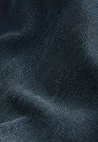Donkere denimstof met een gladde textuur, voorzien van subtiele variaties in tint en een lichte rek, gevouwen om de zachtheid te onthullen.