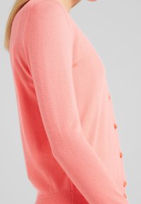 Różowy sweter z dzianiny z długimi rękawami, okrągłym dekoltem i guzikami z przodu. Miękka textura i dopasowany fason.