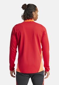Langärmliges Sportshirt in Rot mit orangefarbenen Akzenten, mit rundem Ausschnitt, geschwungener Saum und glattem, elastischem Stoff.