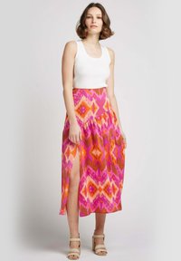 Jupe maxi colorée avec un motif géométrique rose et orange, dotée d'une fente sur le côté, portée avec un débardeur blanc et des talons beiges.