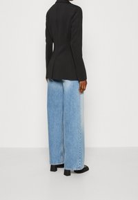 Czarna, dopasowana marynarka z długimi rękawami, zestawiona ze szerokimi, jasnoniebieskimi dżinsami. Jeansy mają przetartą teksturę i są stylizowane z masywnymi czarnymi obcasami.