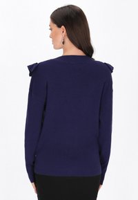 Granatowy, prążkowany sweter z okrągłym dekoltem i dekoracyjnymi kokardkami na ramionach; długie rękawy i lekko zaokrąglony dół z tyłu.