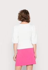 Top branco texturizado com mangas bufantes, combinado com uma saia mini rosa brilhante. Decote redondo simples e detalhes de cintura ajustada.