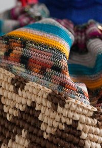 Woven straw basket with a multi-colored fabric lining featuring intricate patterns in orange, blue, and yellow, showcasing rich textures.