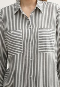 Chemise à boutons rayée grise et blanche avec deux poches poitrine, dotée d'un col et d'un tissu texturé.