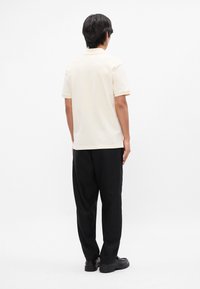 Πόλο μπλούζα κοντομάνικη, ανοιχτού μπεζ χρώματος, με κλασικό γιακά. Φοριέται με χαλαρές μαύρες παντελόνες και μαύρα παπούτσια. Λείος υφασμάτινος ιστός.