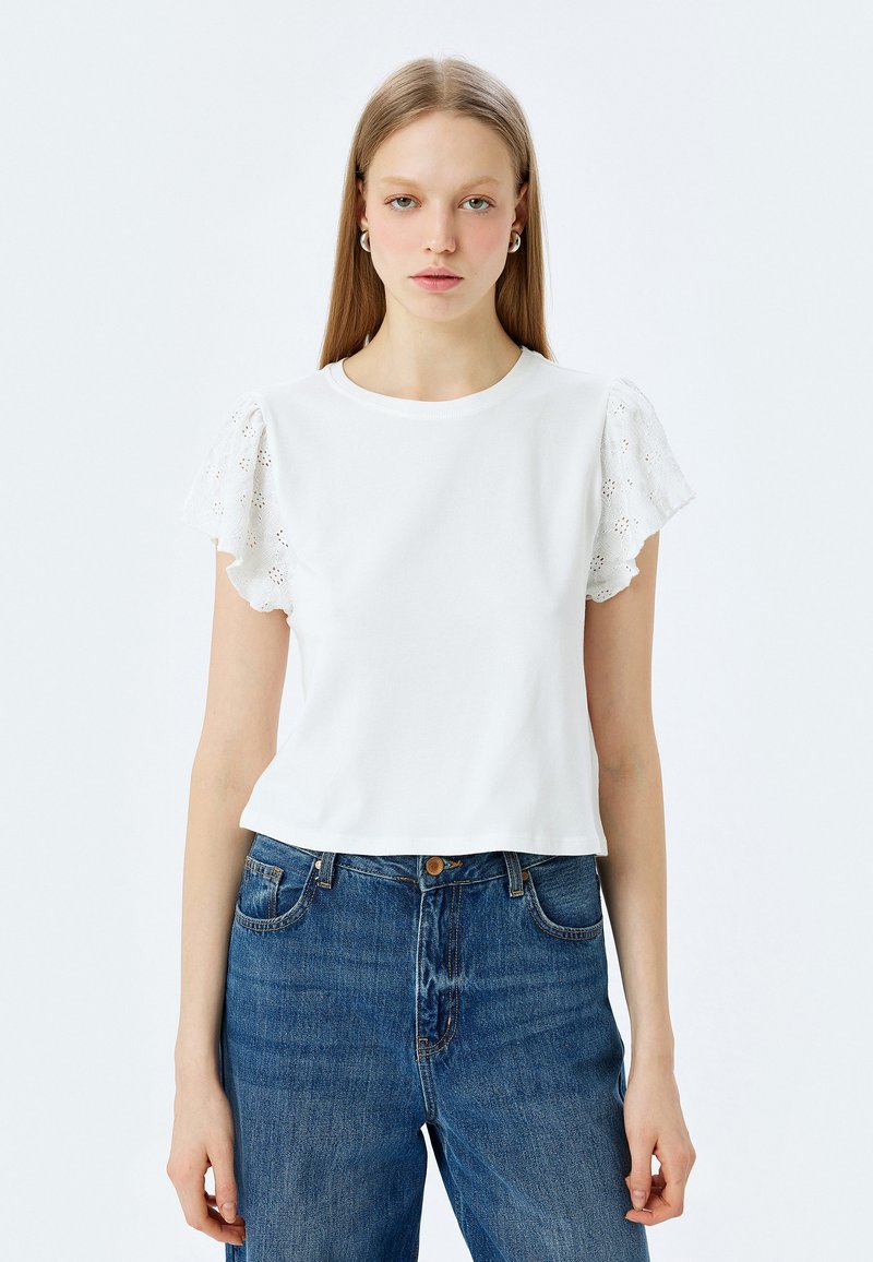 Witte T-shirt met korte mouwen en broderie anglaise details op de mouwen, gecombineerd met hoge taille denim jeans. Glad katoenen textuur.
