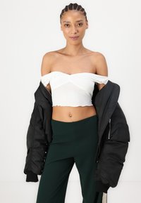 Witte off-the-shoulder crop top met een geribbelde textuur, gecombineerd met hoge donkergroene broek en een zwarte bomberjack.