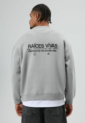 Grijze trui met ronde hals, met zwarte tekst op de achterkant: "RAÍCES VIVAS" en afbeeldingen. Gestructureerde stof met geribbelde manchetten.