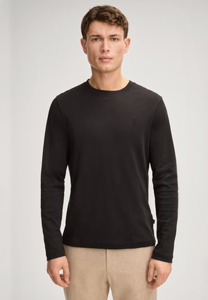 Langärmliges schwarzes T-Shirt aus leichtem Stoff. Hat einen runden Ausschnitt und ein kleines Logo auf der Brust. Einfaches, tailliertes Design.