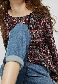 Multikleurige blouse met een gerimpeld ontwerp, ronde hals en lange mouwen, gecombineerd met opgerolde spijkerbroek.